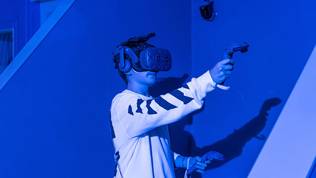 Ein Junge der in einem blauen VR Raum steht und ein VR headset trägt und spielt.