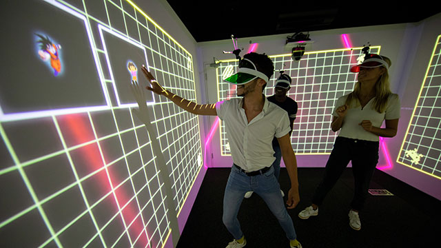 Eine Männer- und Frauengruppe in einer mehrfarbigen LightBox, die ein interaktives immersives Spiel spielen. 
