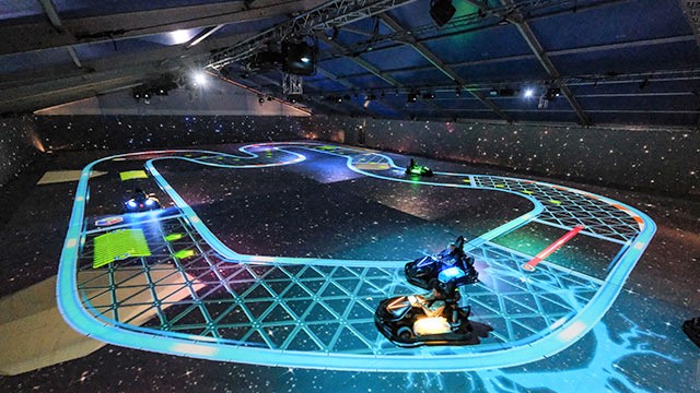 two go-karts racing around a blue futuristic, state-of-the-art race track