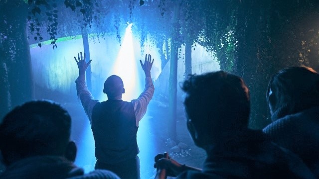 A man standing in front of a blue light from above in a forest