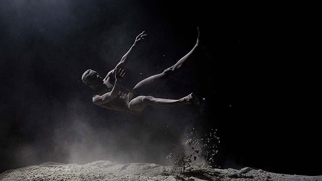 A man falling in mid-air in the dark above the dusty earth 