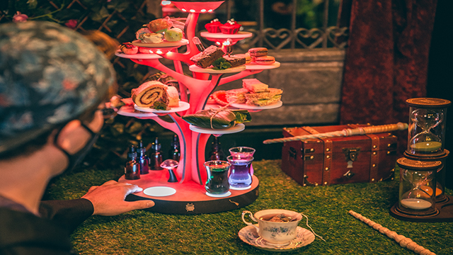 A man touches the afternoon tea stand in form of an pink illuminated tree where are disposed a variety of cakes and a selection of molecular drinks.