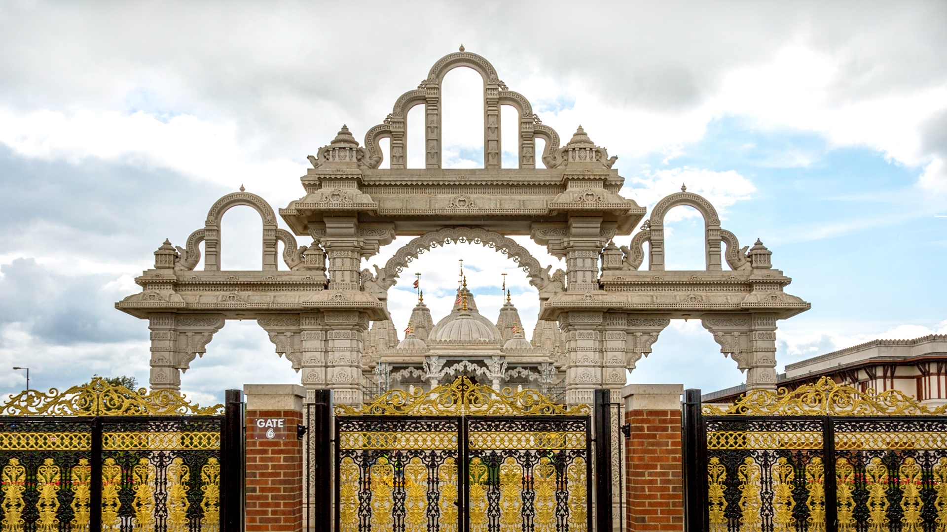 Golden gates in front of Neasdon Temple with a cloudy sky overhead
