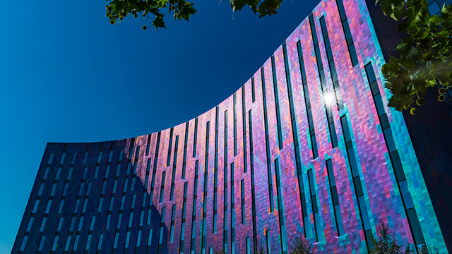 Curved purple and turquoise front of hotel with bright blue sky behind it.