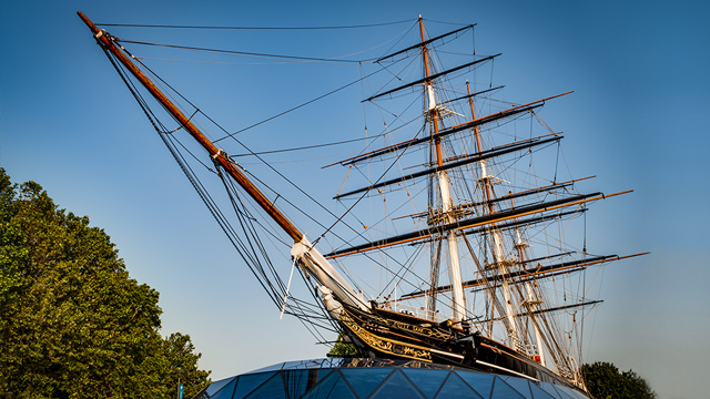 An historic wooden ship viewed from ground level against a blue sky.