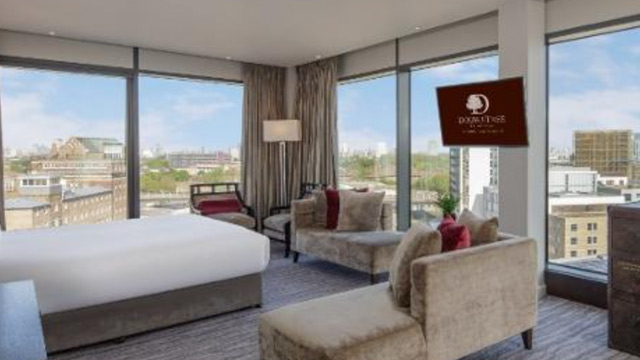 Modern hotel room with wrap-around floor to ceiling windows and a large television screen.