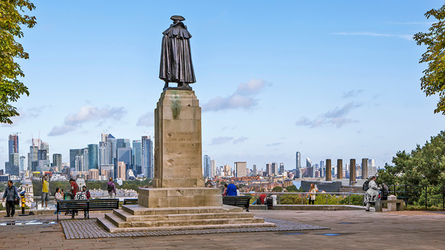 A statue of an historic figure in a cape with the London skyline in the background.