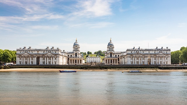 The Old Royal Naval College buildings in Greenwich sit behind shining water.