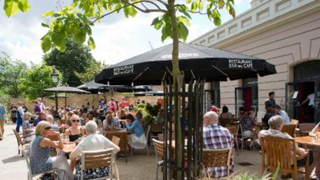 People eating and drinking at wooden tables and chairs on the patio area of a pub.