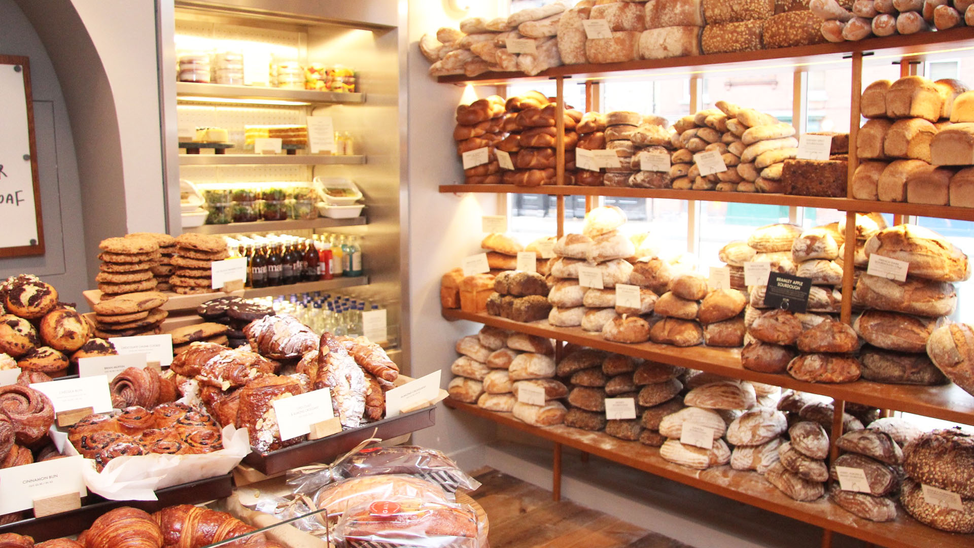 Bakery filled with freshly baked loaves on brown shelves and a counter with croissants and sweet treats.
