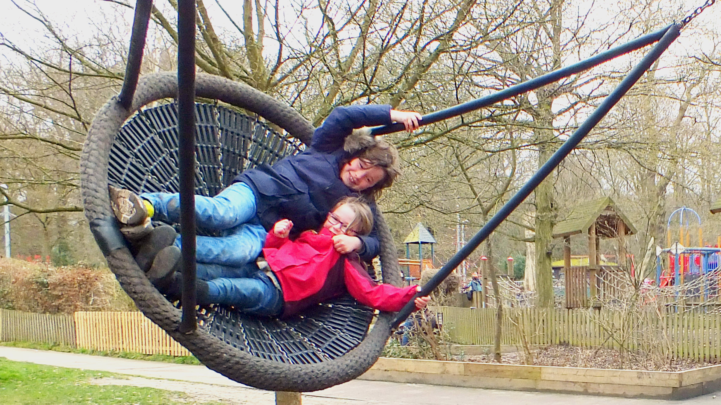 A boy and a girl play on a giant swing wrapped up in winter clothes in Highgate Playground.