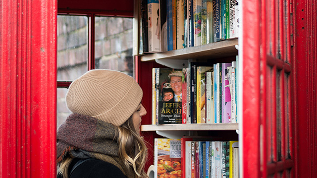 A lady, wearing a beanie hat, studies the books within the phone box library.