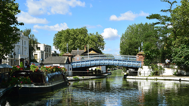 Looking down the canal at Little Venice with a bridge going over the canal and a canal boat on the left, on a sunny day.