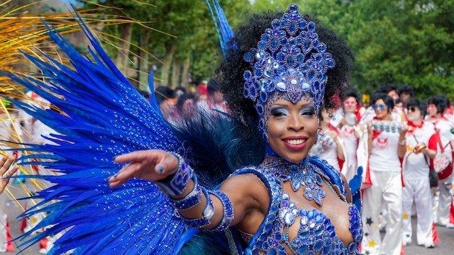 Woman in a blue sequined and feathered costume at Notting Hill Carnival in London.