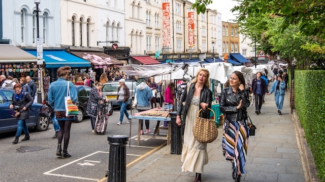Two women walk down Portobello Road, which is filled with market stalls, in London