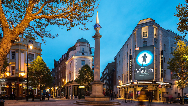 Seven Dials monument surrounded by buildings including the Cambridge Theatre with Matilda the Musical poster.