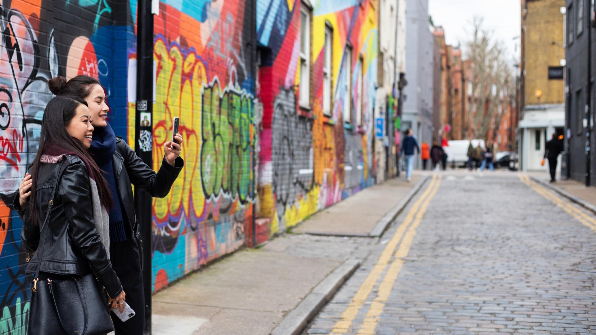 Two women take a selfie in front of colourful street art in a Shoreditch street.