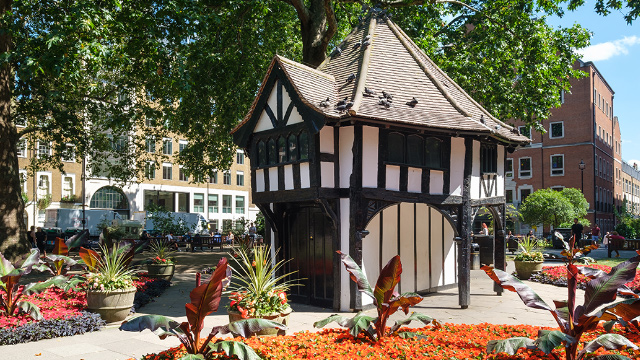 A square in Soho London with trees, plants and a small house in the middle.