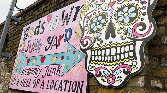 Pink sign on a brick wall reads Gods Own Junk Yard, Heavenly Junk in a Hell of a Location