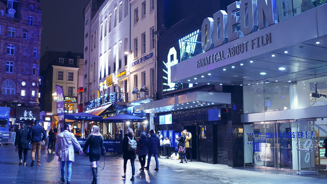 People walking past the Odeon cinema in Leicester Square at night in London's West End.