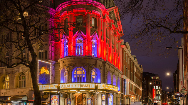 The Aldwych Theatre building lit up in red and purple light at night in London's West End.