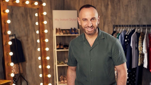 Celebrity stylist Mark Heyes, standing in front of a mirror with lightbulbs, with a rail of clothes and shoes on shelves behind