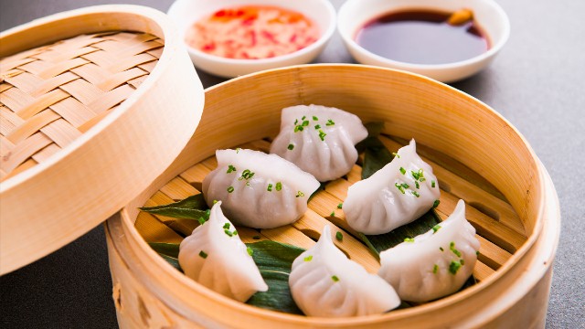 Dim sum cooking class at Ann's Smart School of Cookery. Image courtesy of Red Letter Days. Prawn dumplings in a wooden basket with dipping sauces in the background.