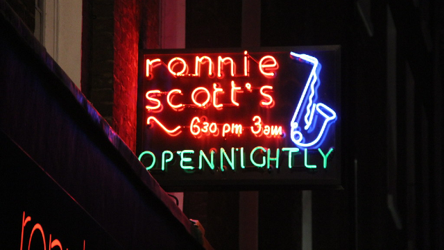 The red neon sign of Ronnie Scott's Jazz Club in Soho lit up during night time.
