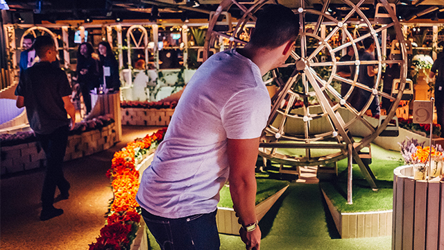 A man lines up a shot at one of Swingers' crazy golf holes, which includes a small wooden version of a big wheel.