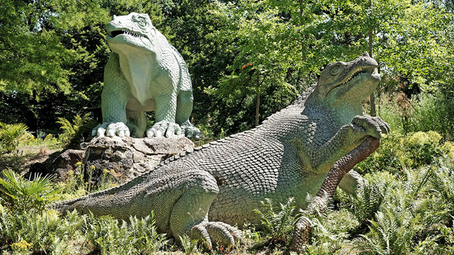 Victorian-era dinosaur sculptures surrounded by greenery in Crystal Palace Park in London.