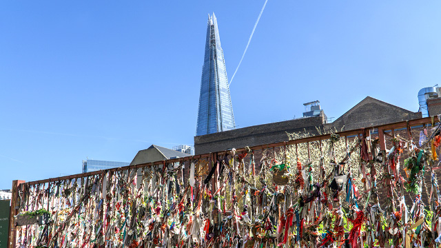 Ribbons on the fence at Crossbones Graveyard, London, on a sunny day with the Shard in the background