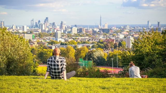 People city on the grass enjoying a view of the city skyline from Parliament Hill in Hampstead Heath in London. © Shutterstock