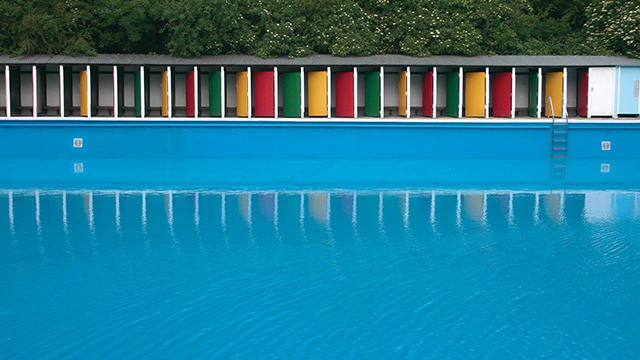 The bright blue lido in the foreground and colourful red, green and yellow doors of the changing rooms in the background.