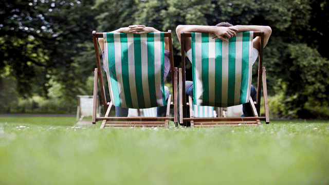 Two images flickering, one of two people sat on stripy deckchairs on grass and facing some shrubbery, and one looking through the hall of a gallery with framed artwork hanging on either wall.