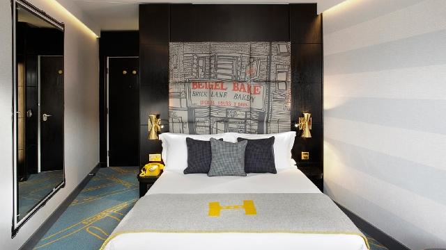 A luxurious double bed in a modern room with bed cover featuring a big mustard letter H.
