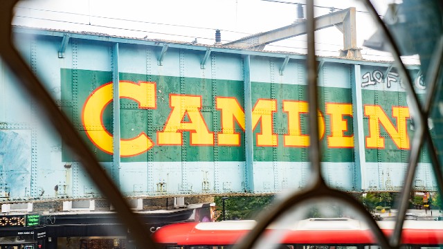 A sign on the side of a bridge that says Camden in large yellow letters against a green background.