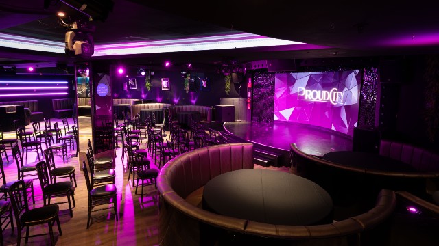 The stage and seating area at Proud Cabaret City, illuminated by a dark pink light.