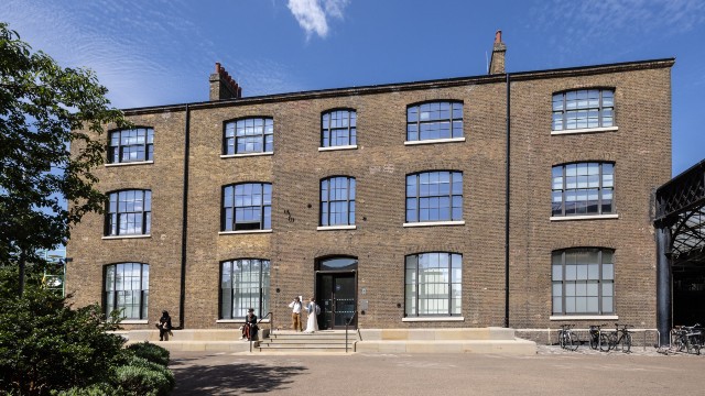 Exterior of large brown brick warehouse-style building with arched windows.