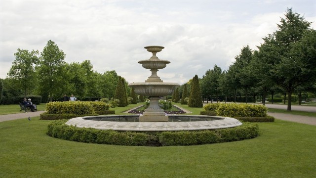 An ornate fountain is in the centre foreground of the image with an avenue of trees shown behind the fountain.