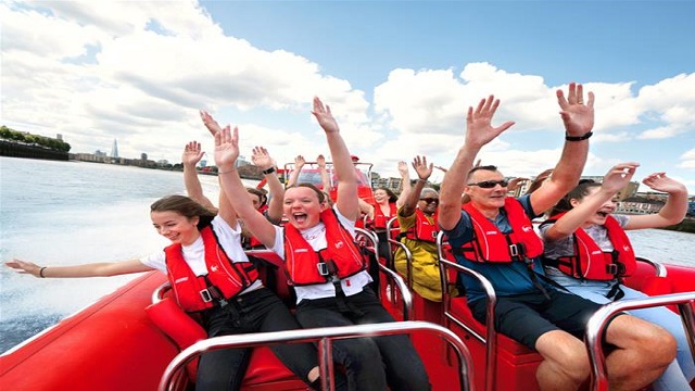 People sat in rows with life jackets on and their hands up on a speedboat trip down a river