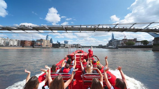 High angle shot of the back of a boat down the Thames, with people having fun with their hands up in the air
