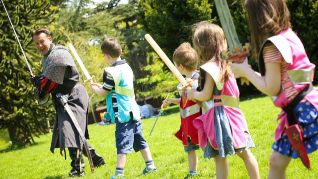 Learn how to wield a sword at Warwick Castle! Image courtesy of Golden Tours. Children are shown how to use a sword by a knight at warwick castle.