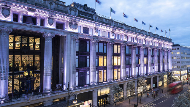 The Selfridges London facade, lit up in pale pink.
