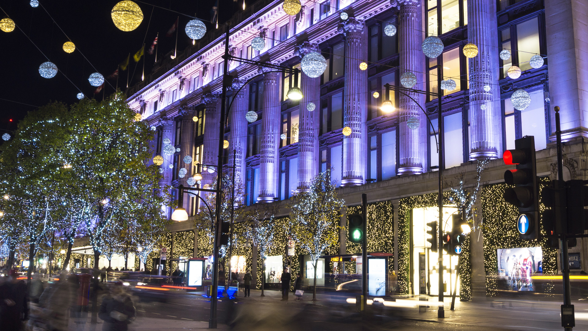 Shoppers and cars pass Selfridges, covered in twinkling lights for the festive season.