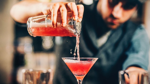 A cocktail mixologist pouring a red cocktail into a glass