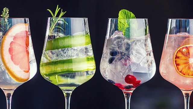 Vier nebeneinander stehende Gin-Gläser, jedes mit bunten Früchten, Eis und Garnitur