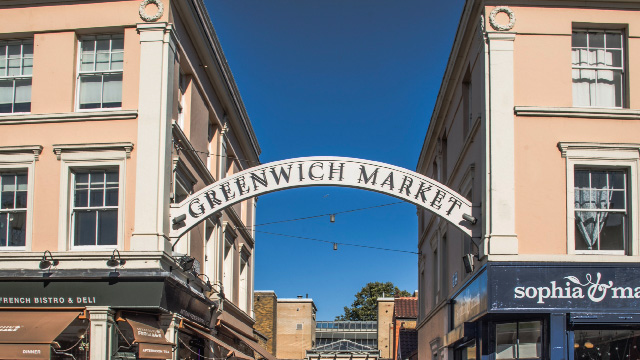 Sign that reads 'Greenwich Market' forms an arch between two buildings on a sunny day