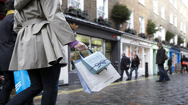 Une femme portant un trench coat se balade sur Newburgh Street à Londres avec quelques sacs après une après midi shopping.