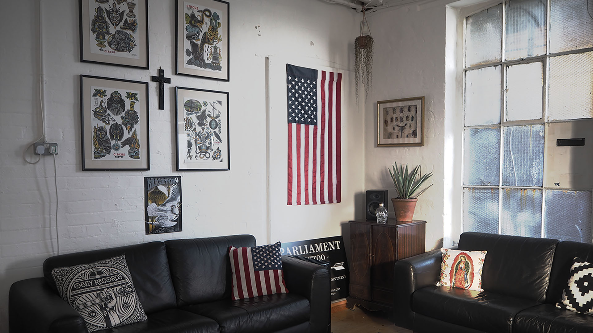 Reception room of Parliament tattoo featuring two leather sofas, drawings of tattoos and an American flag hanging on a white wall.