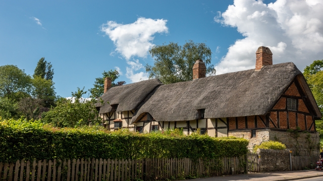 A thatched roof cottage nestled behind a pruned hedge